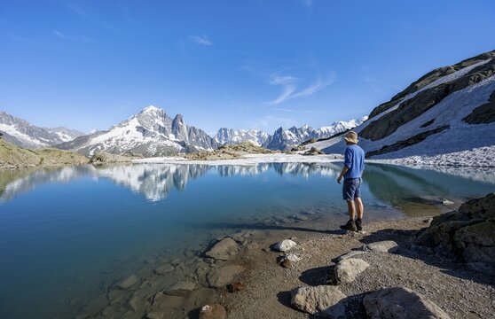 Mountaineer in front of mountain landscape with mountain lake, tourist at Lac Blanc with water reflection, mountain peak Aiguille Verte, Grandes Jorasses, Aiguille du Moine and Mont Blanc, Mont Blanc massif, Chamonix-Mont-Blanc, Haute-Savoie, France