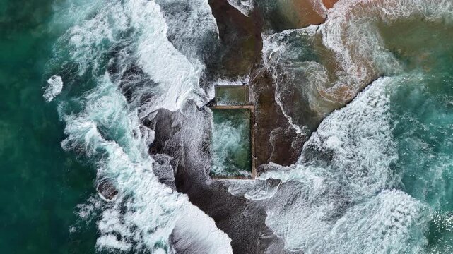 Drone Video aerial view of a beach rock pool on a beach in Sydney Australia and waves crashing on the pool 