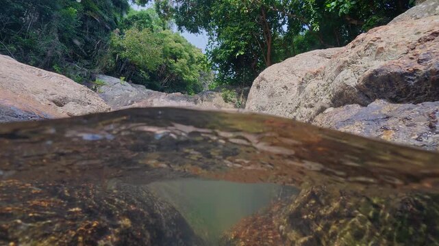 Half underwater view in a natural pool at Na Muang Waterfall 2 on Koh Samui, Thailand. Split level perspective reveals crystal clear freshwater below the surface and tropical rainforest