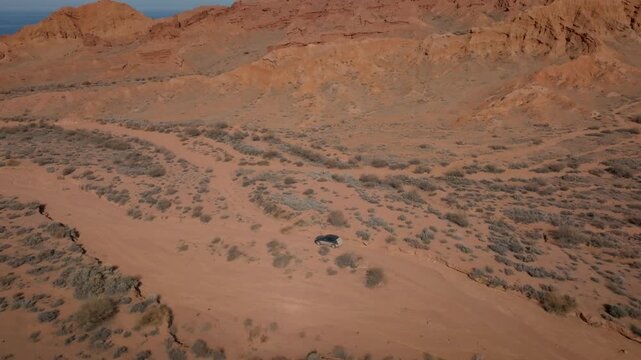 Drone footage of red sandstone cliffs and arid desert valley with a lone car on a dirt road at Mars Canyon, Issyk-Kul Region, Kyrgyzstan