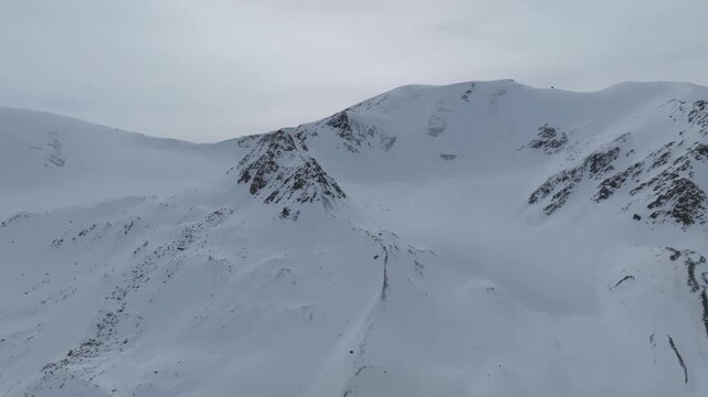 Drone view of rugged snow-covered peaks and ridgelines on Arabel Plateau in Issyk-Kul Region, Kyrgyzstan, under an overcast sky, pristine alpine wilderness