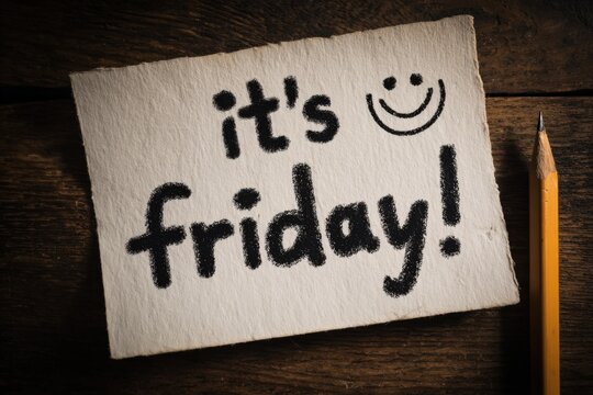 Handwritten note on textured paper stating "it's friday!" with a smiley face, accompanied by a yellow pencil on a rustic wooden surface