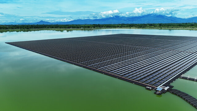 Aerial view of a massive sprawling floating solar farm on a green water reservoir with mountains under a cloudy sky.