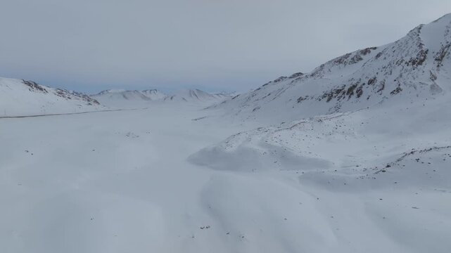 Aerial winter view of the snow-covered Arabel Plateau with rugged mountain ridges and wide valley under overcast sky, remote highlands of Issyk-Kul Region, Kyrgyzstan