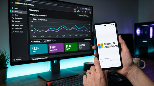 Person using Microsoft Advertising platform on desktop and mobile phone to track campaign performance, pay per click data and marketing analytics.