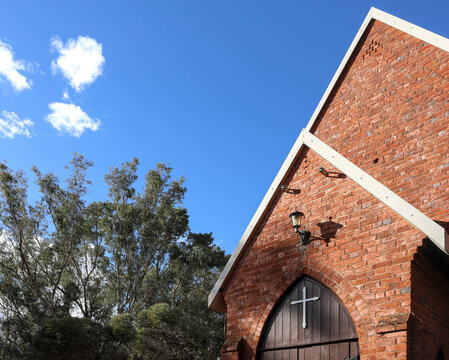 Historic red brick church. Wooden entrance door, with cross. Serenity and Faith. Rustic Architecture, rural Australia. Traditional Christian church exterior. Copy space