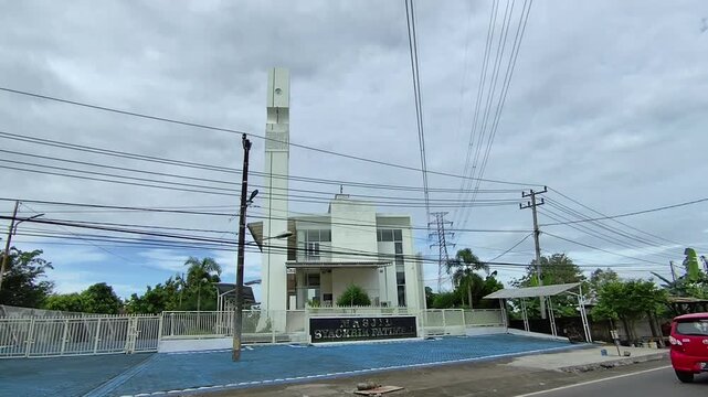 Makassar, 14 April 2024 - Footage of a modern white mosque featuring a tall minaret, contemporary architecture, and an urban setting beneath a cloudy sky.