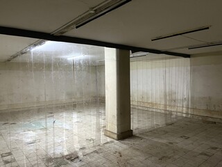 Naklejka premium Spacious underground facility featuring concrete support columns, tiled flooring, and fluorescent illumination within an aging building structure.