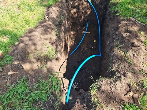Laying underground blue plastic water pipes in a dirt trench. Construction of residential water supply, utility pipeline installation, plumbing works in the earth.
