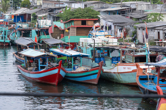 Cilacap, Indonesia - May 15, 2026: High-angle view of traditional wooden fishing boats moored at a fishing port beside a densely populated waterfront settlement.