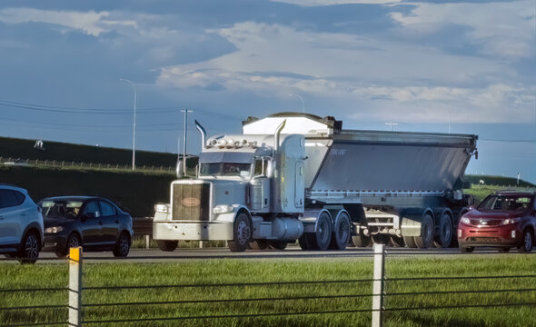 Calgary, Alberta, Canada. June 7, 2026. Side view of a white semi-truck hauling a gravel trailer down a highway alongside passenger cars.
