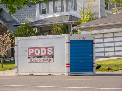 Calgary, Alberta, Canada. June 7, 2026. A white and blue PODS moving and storage container sits parked on a suburban residential street.