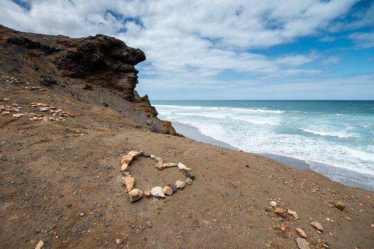 Sunny summer coast with heart stone circle on sandy cliff