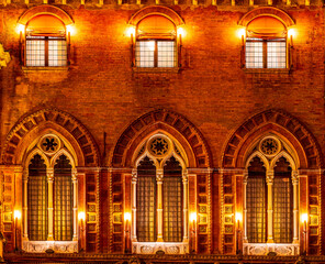 Obraz premium old yellow facade of house with three brown vintage windows in retro gothic italian european style. Night italian architecture.