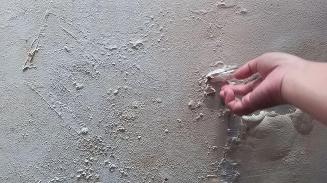 Close up of a hand peeling off damaged bubbly paint from a damp concrete wall during home renovation