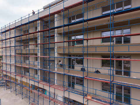 Workers repair a building using scaffolding in a city neighborhood
