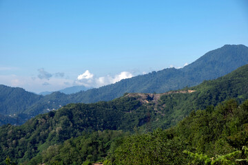 Obraz premium Mountain landscape with green forested slopes and light clouds under a blue sky in Adjara, Georgia