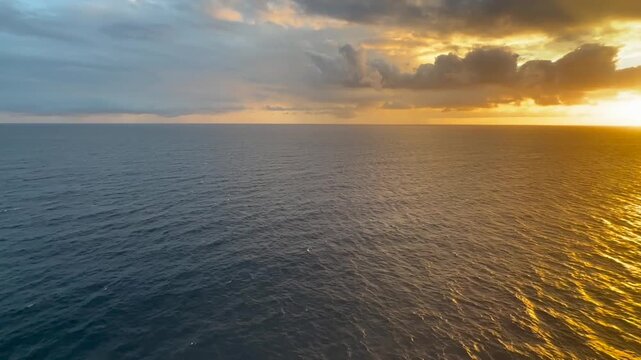 Stunning aerial view of the Caribbean Sea at golden sunset, filmed from the upper deck of a cruise ship near Saint Kitts Island. The warm colors of the setting sun reflect across the calm ocean surfac