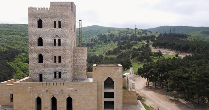 Aerial drone pull-away shot of the large Derbent sign and stone watchtower monument on a green hill