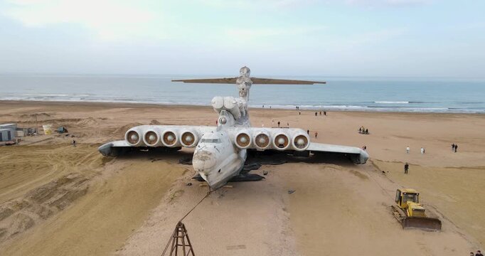 Cinematic aerial orbit shot of the abandoned Soviet Lun-class ekranoplan nose and jet engines on the Caspian Sea coast near Derbent