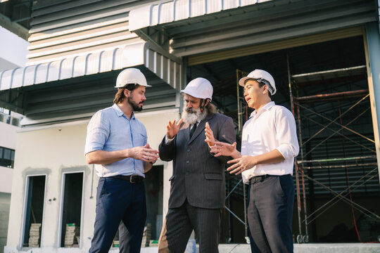 Investor engineers talking outside empty factory warehouse construction site, Three people in white hard hats converse near a building under construction, Customer service or investors planning.
