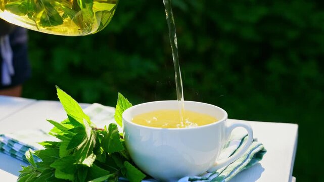 Herbal mint tea being poured into a white cup outdoors