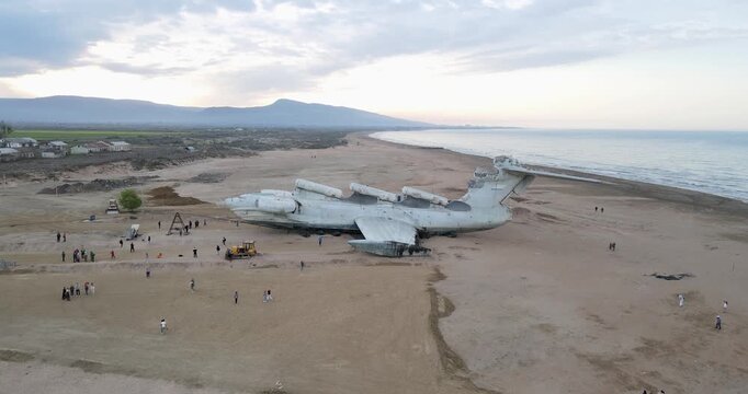 Aerial drone pull-away shot of the abandoned Soviet Lun-class ekranoplan on the Caspian Sea coast at sunset