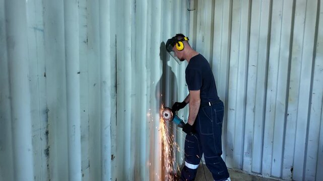 Worker cutting shipping container wall with angle grinder