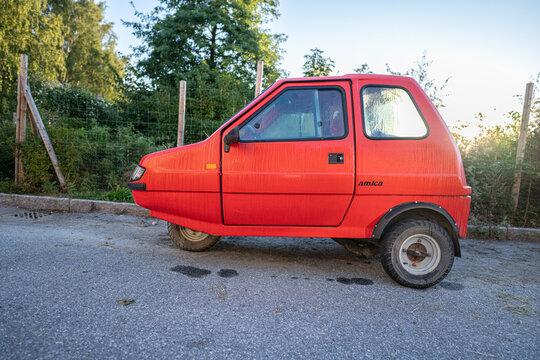 Gothenburg, Sweden - september 20 2024: Small red urban microcar parked beside fence at sunrise.