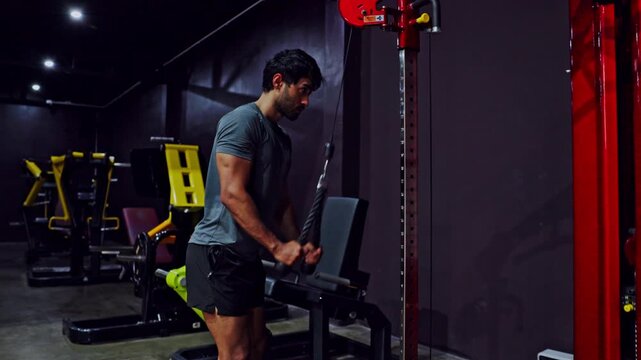 Focused young man fitness exercise in gym cable machine workout, training arm triceps with rope attachment, strength routine muscle conditioning athletic lifestyle