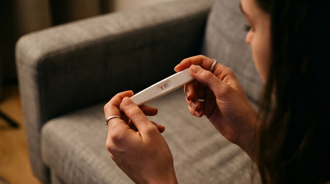 Close up of woman holding pregnancy test device on sofa