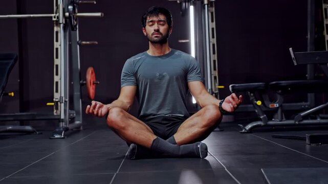 Man meditation gym fitness exercise seated calm strength training wellness athlete cross leg pose on floor equipment background mindful breathing modern health club interior