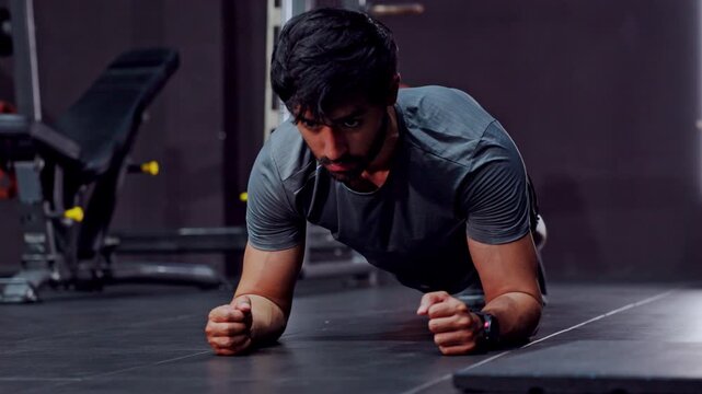 Focused man plank exercise gym fitness workout strength training core endurance on floor in dark indoor space building stability during intense athletic session