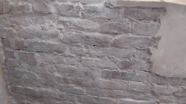Slow camera tilt of an old white painted brick wall with cracked and peeling plaster texture