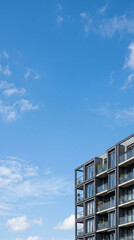 Fototapeta premium Minimalist architectural detail of a modern apartment building with dark facade and glass balconies, set against a vast blue sky with ample copy space for text.