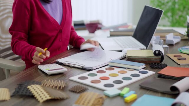 Asian woman furniture designer selecting color palette material samples working with laptop notebook creative professional planning interior design project at