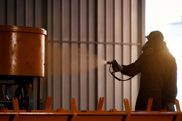 Fototapeta premium Industrial painter spray painting yellow coating on machinery metal parts, waring protective suit respirator mask spray painting yellow coating heavy machinery metal equipment factory workshop.