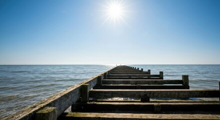 Fototapeta premium Wooden pier stretches into the ocean under a bright, sunny sky