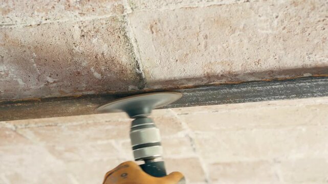 Worker using a tuckpointing grinder to remove rust from the ceiling beam.