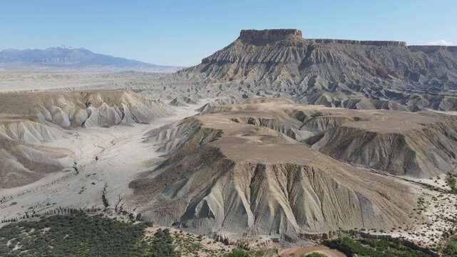 Cinematic 4K drone footage flying horizontally to the right over the dramatic eroded clay badlands of Utah, with Factory Butte in the background. Smooth uniform movement at 60fps, easily reversible.