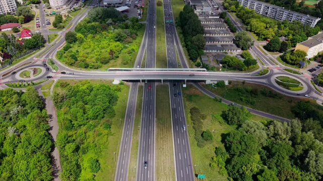 Multi lane highway overpass drone view city traffic road junction green trees. This high-angle aerial shot captures vehicles driving along a modern multi-lane freeway with complex intersections and ro