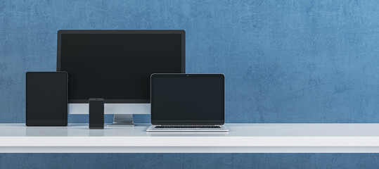 Naklejka premium Modern digital device set featuring computer monitor, laptop, tablet and smartphone arranged on clean desk against textured blue background for technology branding. 3D Rendering