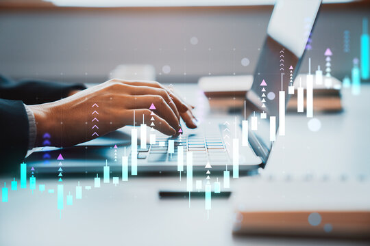 Hands typing on laptop with financial chart overlays in modern business workspace, showing digital trading analytics background.