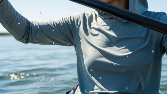 Person wearing grey sun shirt paddling kayak on calm lake water.