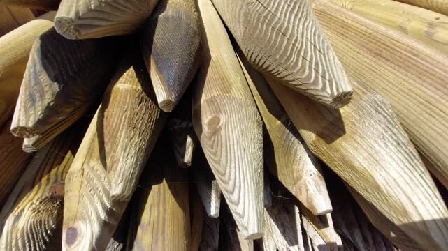 Close-up shot of a stack of sharpened wooden fence posts and stakes drying in the sun