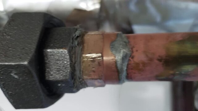 Horizontal tracking shot of a copper pipe connection with a large black nut and red valve lever