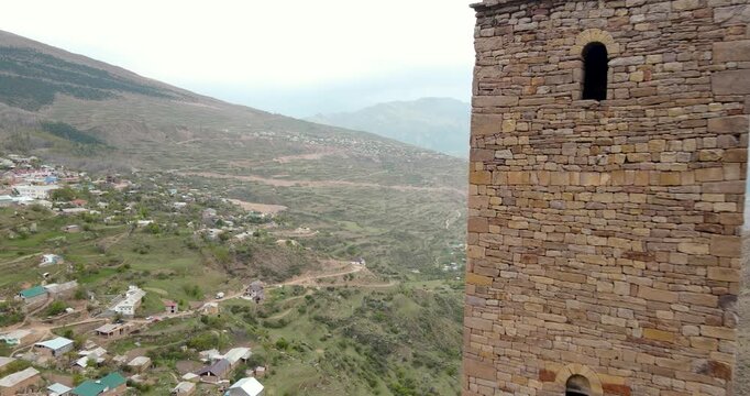 Aerial drone pull-away shot of an ancient stone watchtower revealing a scenic mountain village in Kahib, Dagestan
