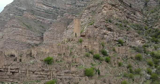 Aerial drone boom up shot of the ancient abandoned stone village and watchtower ruins built on cliffs in Kahib, Dagestan