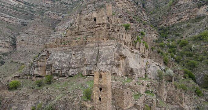 Aerial drone boom up shot of an ancient defensive stone watchtower built on a steep cliff in the ruined village of Kahib, Dagestan
