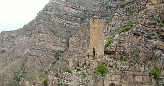 Cinematic aerial orbit shot of the ancient defensive stone watchtower and surrounding village ruins in Kahib, Dagestan